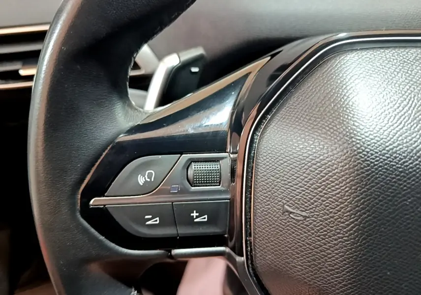 Gros plan sur le côté gauche du volant cuir noir du Peugeot 3008 gris foncé, avec commandes audio intégrées.