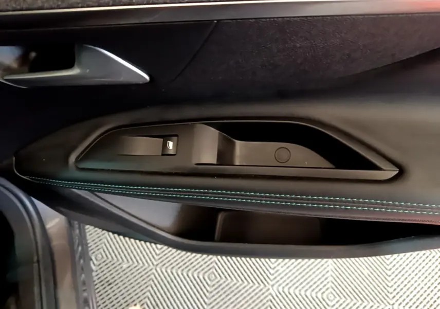 Détail de la porte côté gauche du Peugeot 3008 gris foncé, avec bouton de lève-vitre et surpiqûres bleues.