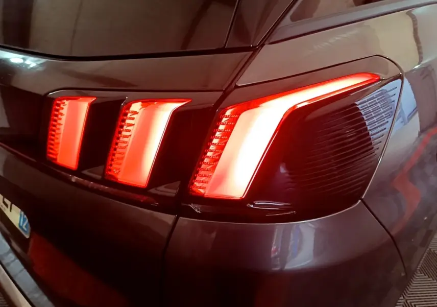 Gros plan sur le feu arrière droit allumé d’un Peugeot 3008 gris foncé, soulignant son design en trois griffes lumineuses.