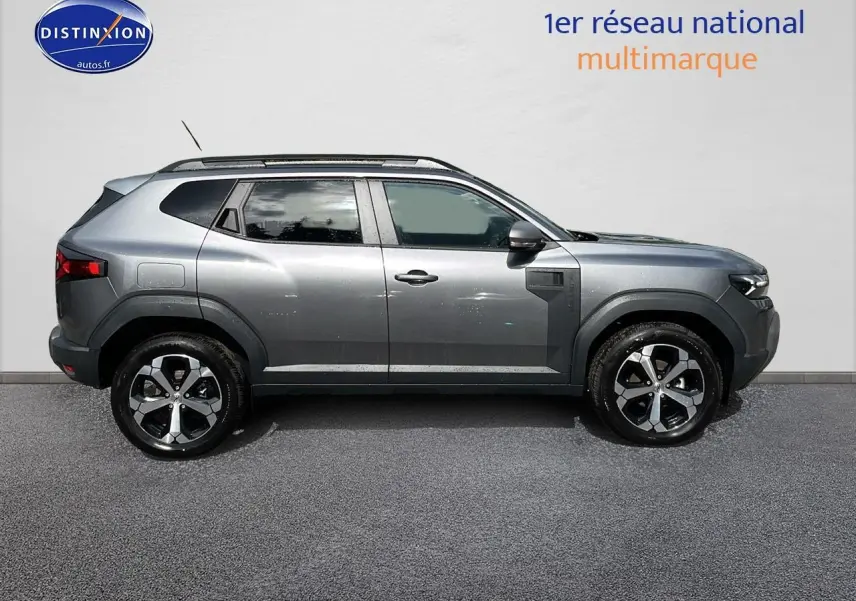 Profil droit du Dacia Duster gris schiste 2025 avec jantes alu et barres de toit visibles sur fond neutre.