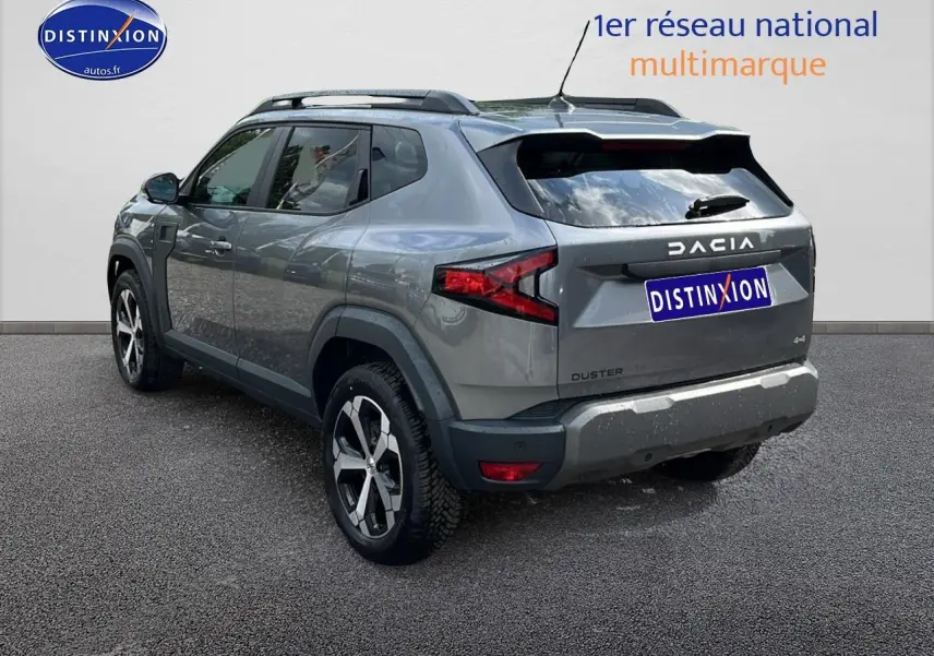 Dacia Duster gris schiste vu en 3/4 arrière droit, avec barres de toit et jantes alu distinctives.