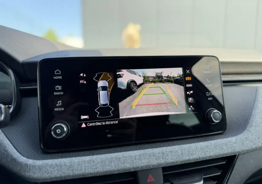 Écran central affichant la caméra de recul avec vue arrière d'une Skoda Scala blanc glacier en stationnement.