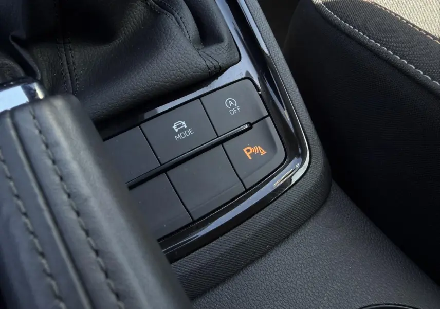 Gros plan sur la console centrale noire de la Skoda Scala TSI 116 Sélection, avec boutons de mode de conduite et aide au stationnement.