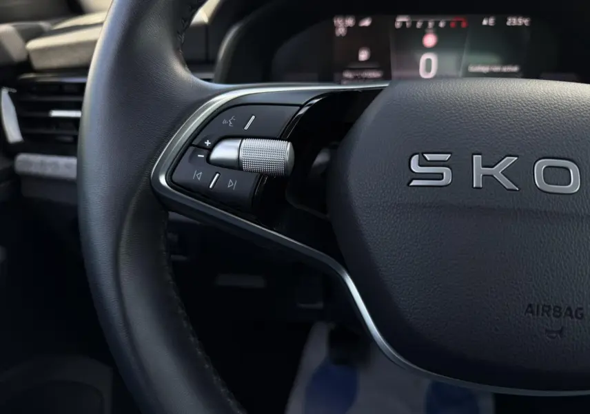 Gros plan sur le volant cuir noir de la Skoda Scala TSI 116, avec commandes multifonctions et tableau de bord digital flou en arrière-plan.