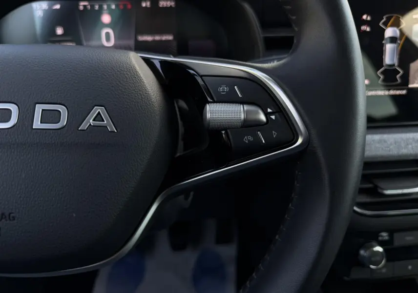 Gros plan sur le volant cuir noir de la Skoda Scala TSI 116, avec commandes multifonctions et tableau de bord numérique en arrière-plan.