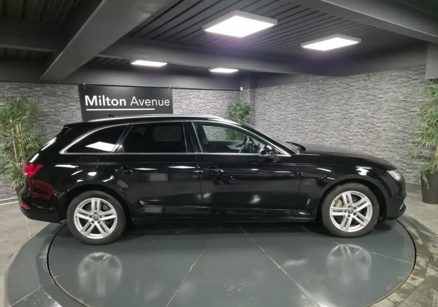 Audi A4 Avant noire vue de profil côté gauche dans un showroom avec jantes aluminium 17 pouces et rétroviseurs noirs brillants.