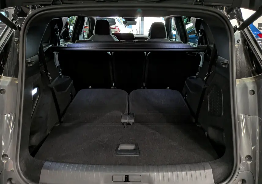 Coffre ouvert vu de l'arrière d'un Peugeot 5008 Hybrid gris titane avec sièges arrière rabattus et toit noir visible.