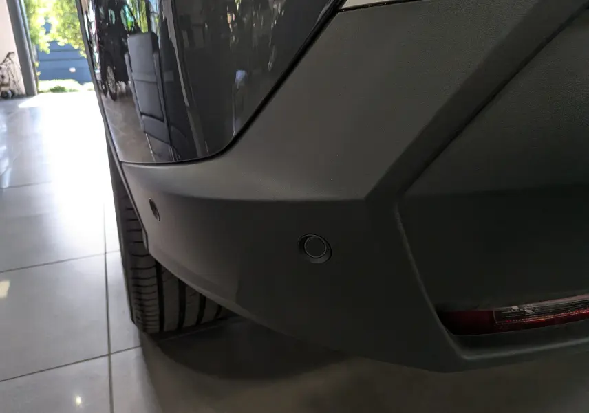 Gros plan sur le pare-chocs arrière gris titane du Peugeot 5008 Hybrid 145 GT avec capteurs de stationnement visibles.