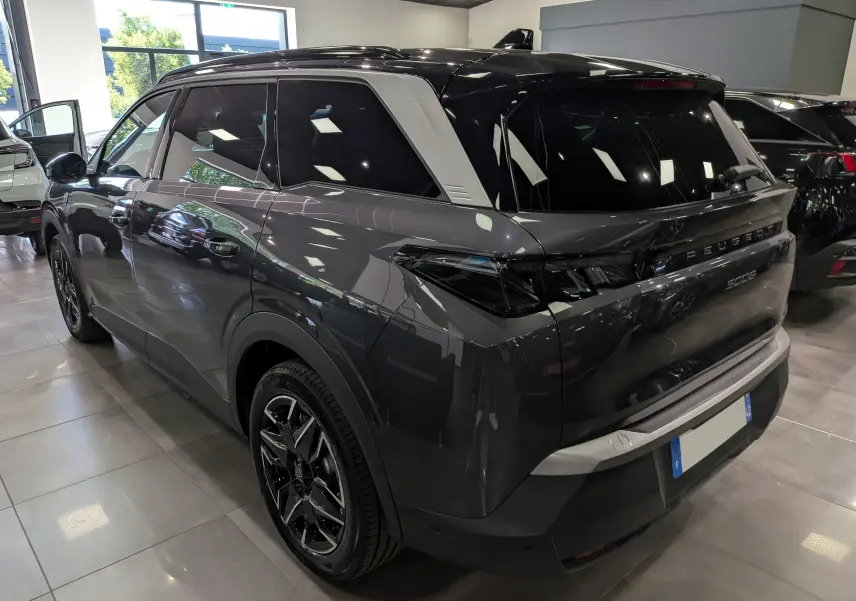 Vue 3/4 arrière droite du Peugeot 5008 Hybrid gris titane avec toit noir et jantes biton dans un showroom.