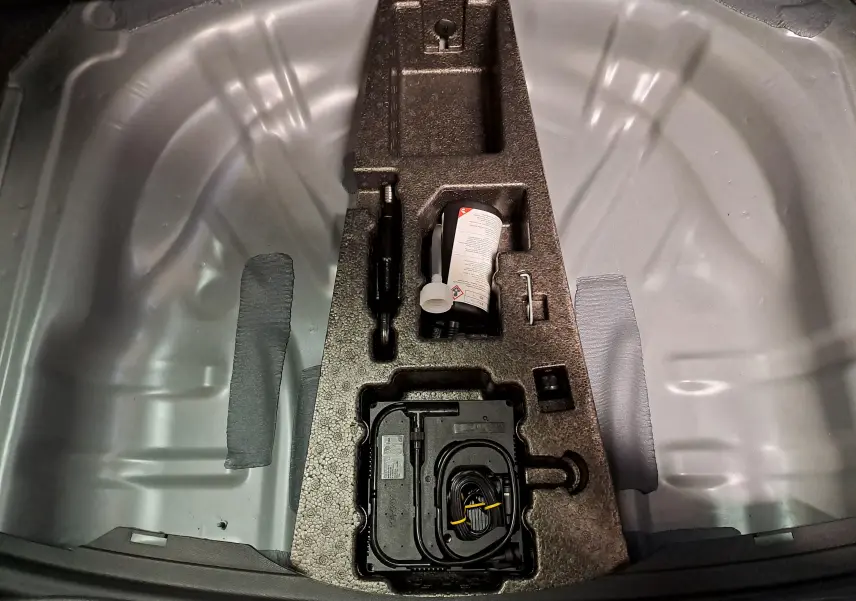 Vue plongeante sur le coffre ouvert d'une SEAT LEON gris magnétique, montrant le rangement d'outils et compresseur intégré.