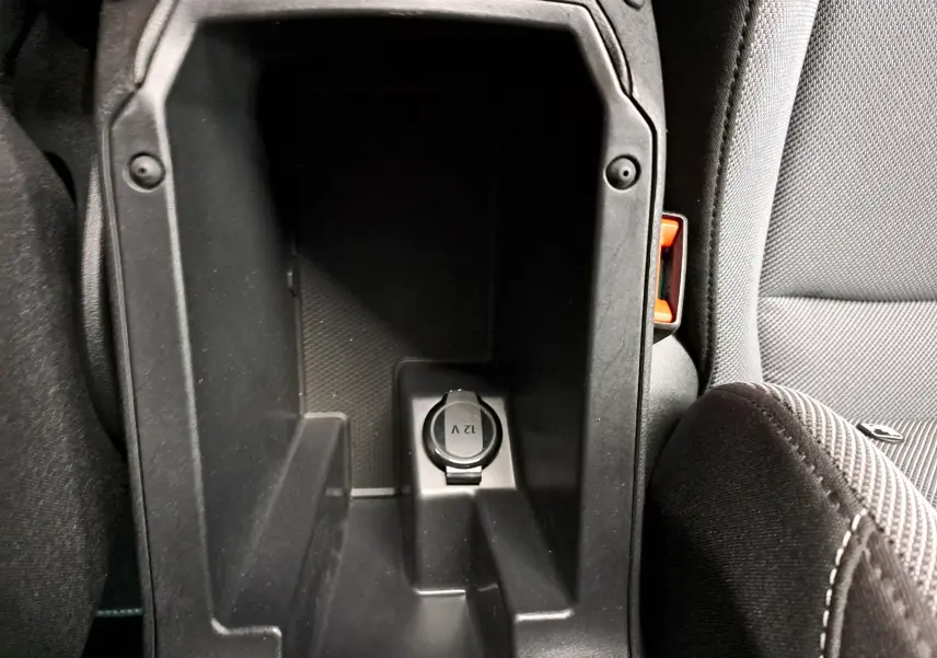 Gros plan sur la prise 12V dans l'accoudoir central noir du SEAT LEON 1.5 eTSI Hybrid gris magnétique, intérieur tissu gris.