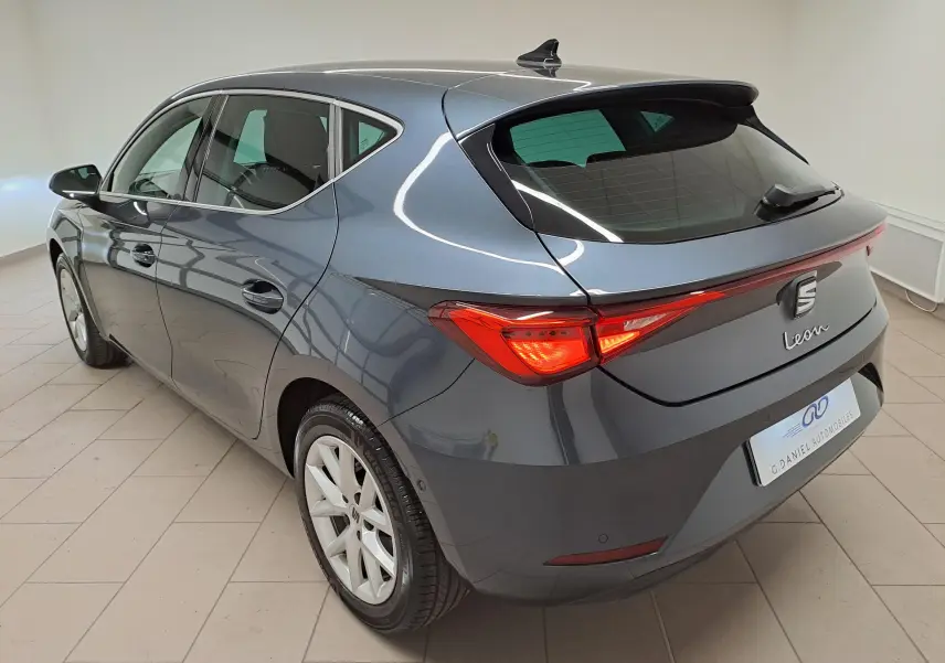 Vue 3/4 arrière droite d'une SEAT Leon 1.5 eTSI Hybrid gris magnétique avec vitres arrière surteintées et rétroviseurs rabattables.