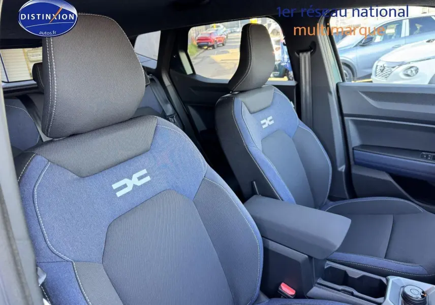 Vue intérieure des sièges avant bleu et noir du Dacia Duster 2025 avec accoudoir central et logo distinctif brodé.