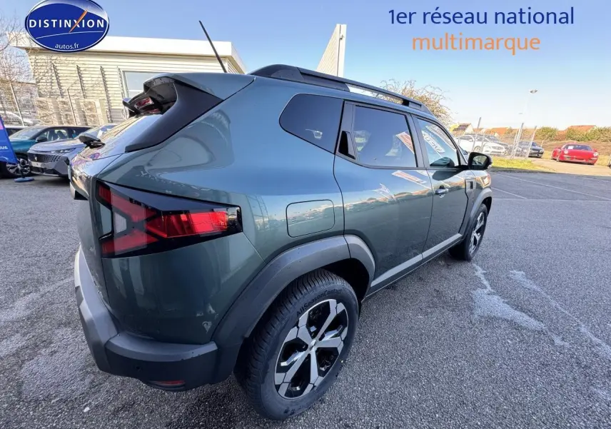 Vue 3/4 arrière droite d'un Dacia Duster 2025 vert cèdre avec barres de toit et jantes alu noires.