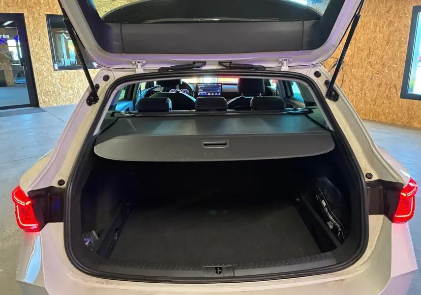 Vue arrière ouverte sur le coffre spacieux d'une CUPRA LEON ST blanche 2024, avec cache-bagages et sièges noirs visibles.