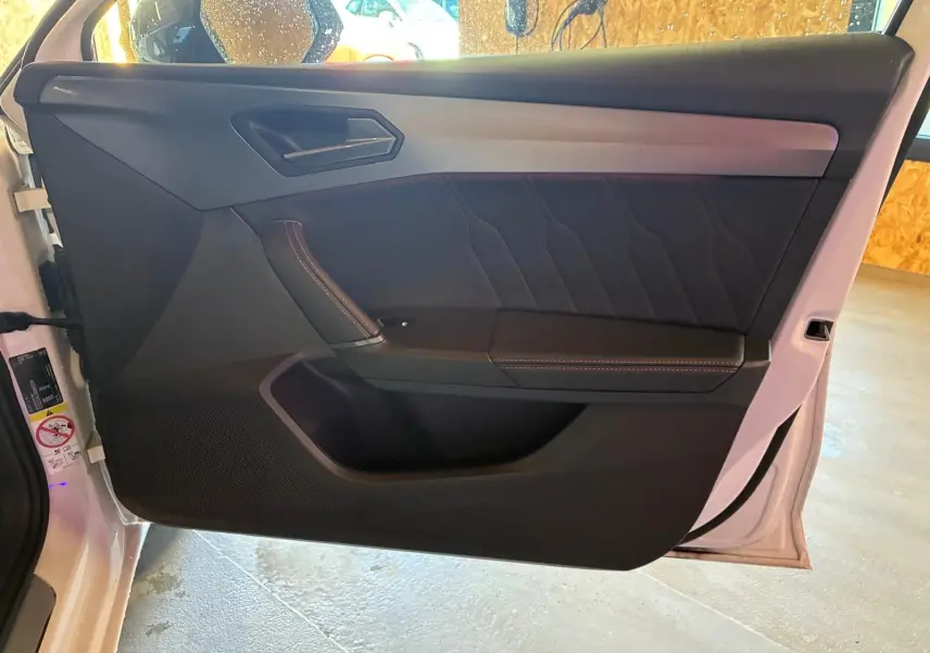 Vue intérieure de la porte avant gauche blanche d'une CUPRA LEON ST 2024 avec garniture noire et surpiqûres contrastées.