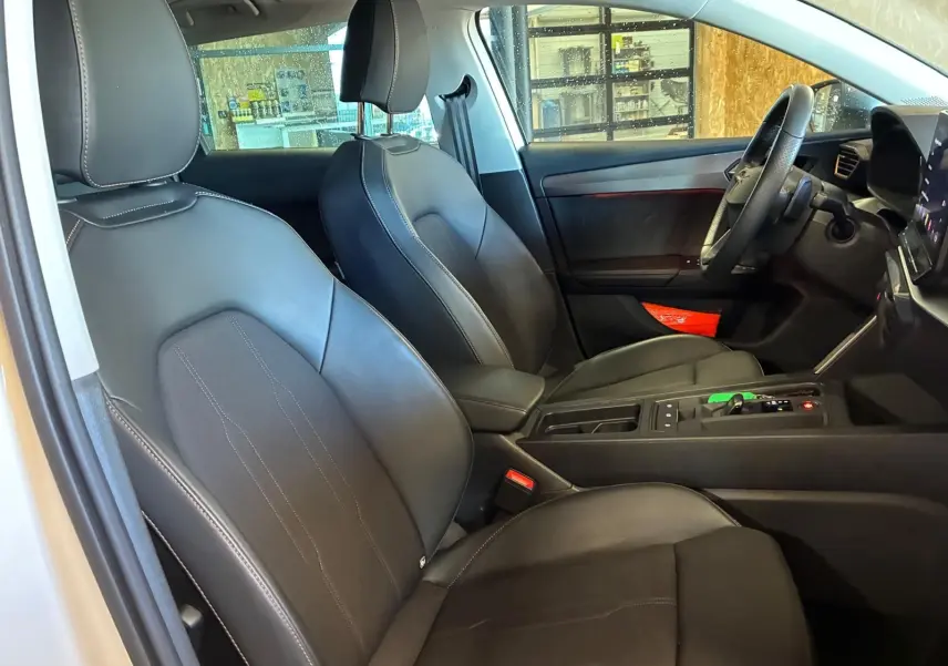 Vue intérieure côté conducteur de la CUPRA LEON ST 2024, sièges noirs avec surpiqûres blanches et console centrale moderne.