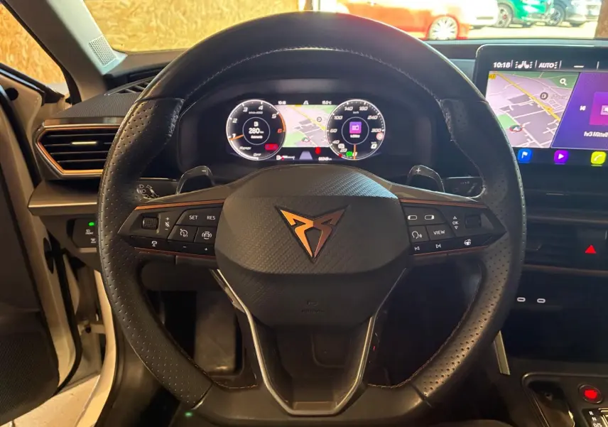 Vue intérieure centrée sur le volant noir perforé avec logo CUPRA et tableau de bord digital lumineux.