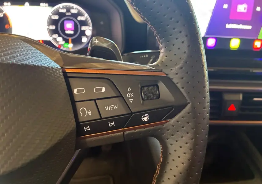 Gros plan sur le volant perforé noir de la CUPRA LEON ST 2024 avec commandes multifonctions et tableau de bord numérique.