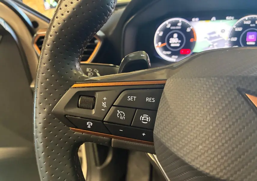 Gros plan sur le volant perforé noir de la CUPRA LEON ST 2024 avec commandes de régulateur et tableau de bord numérique.