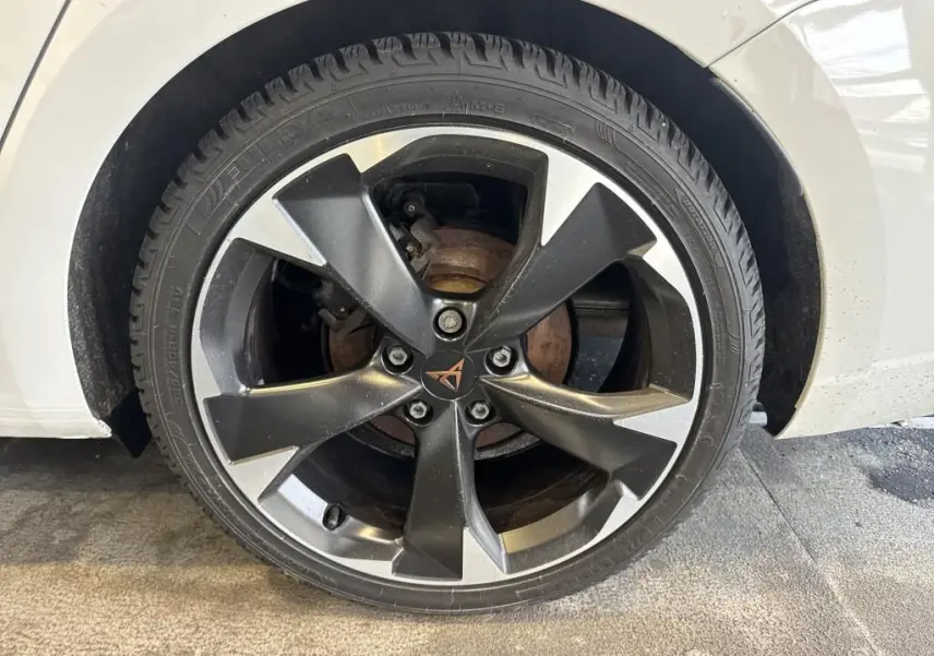 Gros plan sur la roue avant droite d'une CUPRA LEON ST blanche, mettant en valeur la jante alliage noire et argentée au logo CUPRA central.