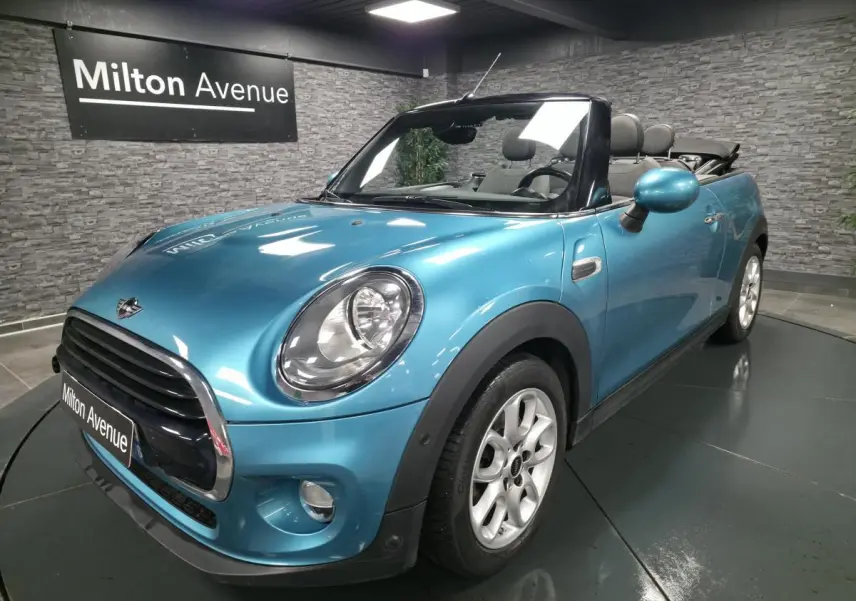 MINI Cabriolet bleu vue 3/4 avant droit, capote ouverte et jantes argentées visibles en intérieur showroom.