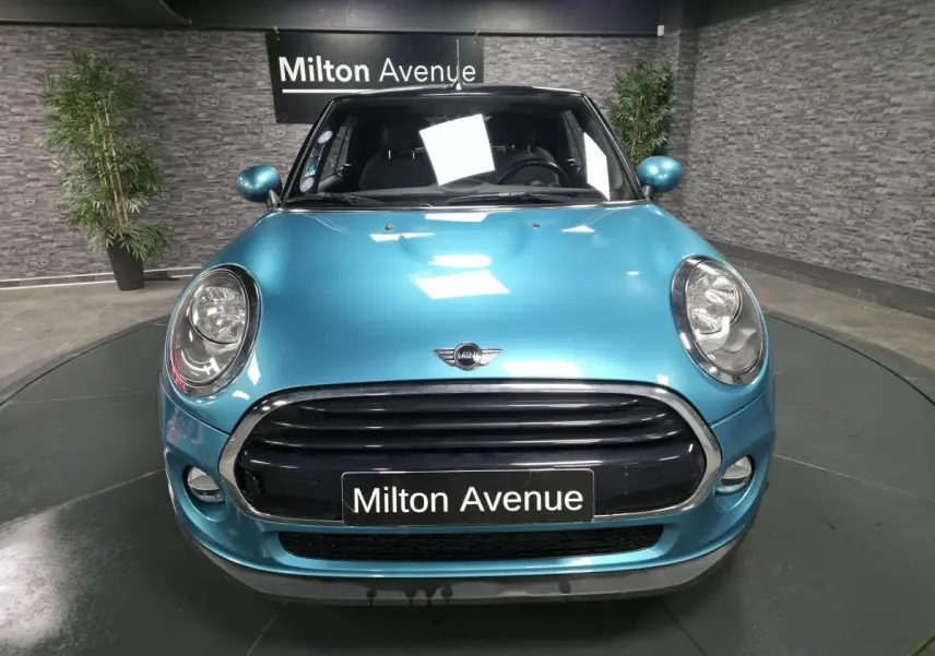 Vue avant d'une MINI Cabriolet bleu métallisé avec calandre noire et logo MINI sur capot, en intérieur showroom.