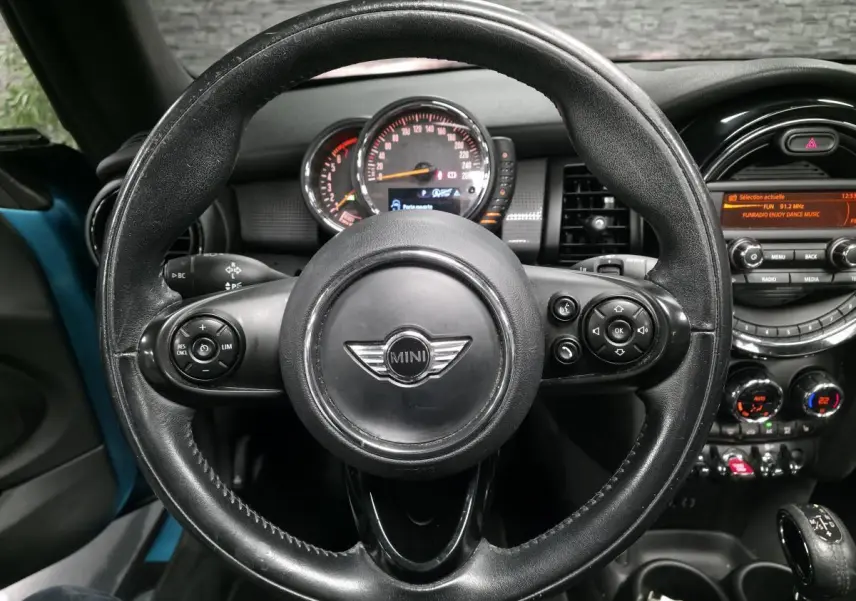Vue centrée sur le volant en cuir noir d'une MINI Cabriolet bleu, avec tableau de bord et console centrale visibles.