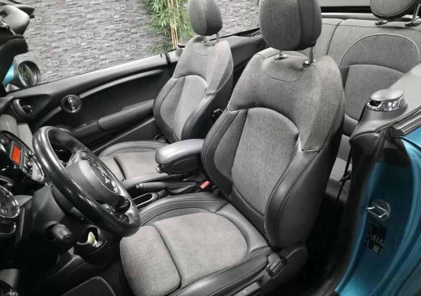 Vue intérieure côté conducteur d'un MINI Cabriolet bleu 2017, sièges avant tissu gris et cuir noir avec volant cuir.
