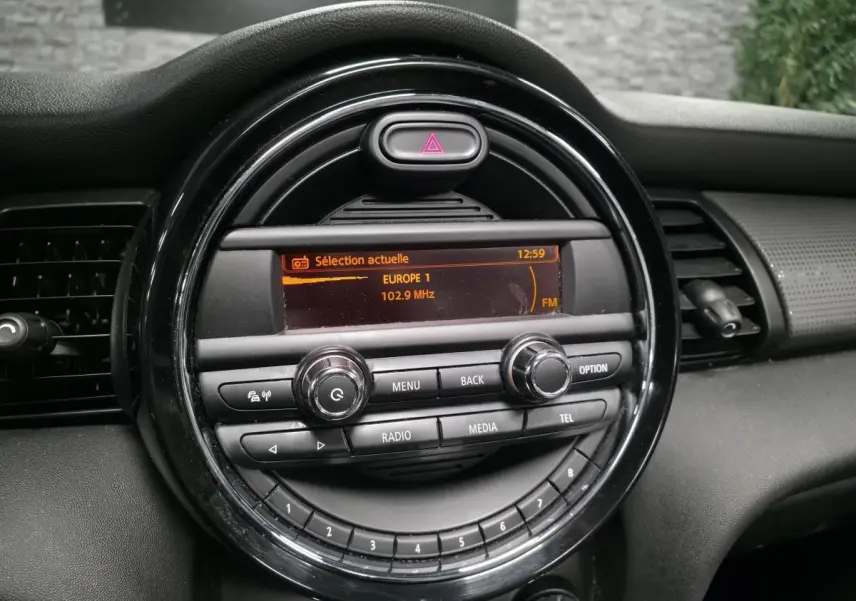 Gros plan sur la console centrale noire du MINI Cabriolet bleu, affichant l'autoradio réglé sur Europe 1 à 102.9 MHz.