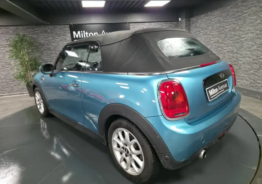 Vue 3/4 arrière droite d'une MINI Cabriolet bleu avec capote noire et sortie d'échappement chromée visible.