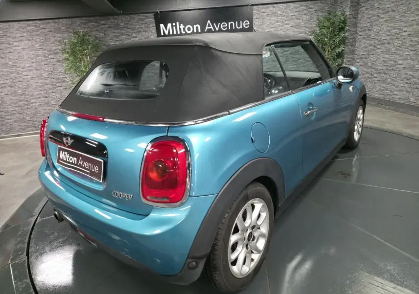 Vue 3/4 arrière droite d'une MINI Cabriolet bleu avec capote noire et feux arrière rouges, stationnée en intérieur.