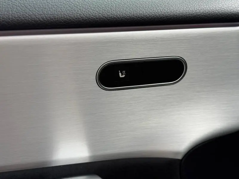 Gros plan sur le bouton de siège chauffant intégré dans la garniture aluminium brossé intérieur gris d'une Mercedes Classe A 200 d AMG Line.