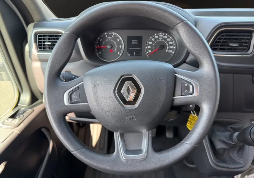 Vue rapprochée du volant noir Renault Master 2023 avec tableau de bord et commandes visibles en arrière-plan.
