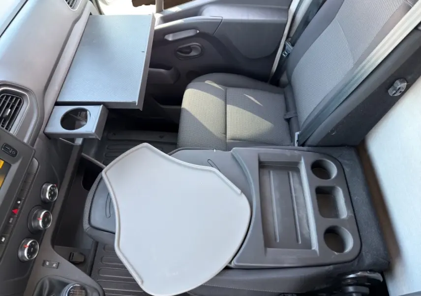 Vue intérieure côté passager du Renault Master 2023, montrant siège gris avec tablette rabattable et rangements intégrés.