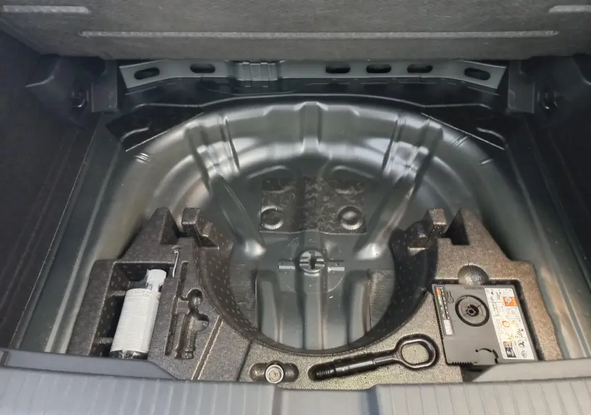 Coffre ouvert du Volkswagen T-Roc 2025 gris Indium, vue sur le rangement sous plancher avec kit de réparation pneus.