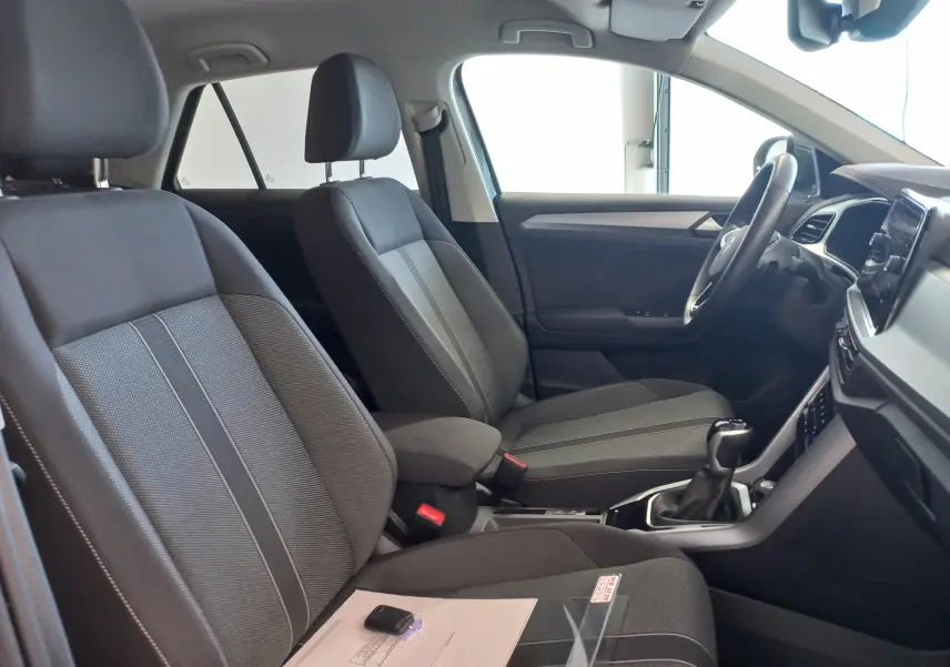 Vue intérieure côté gauche du Volkswagen T-Roc 2025, sièges tissu gris avec console centrale et volant visibles.