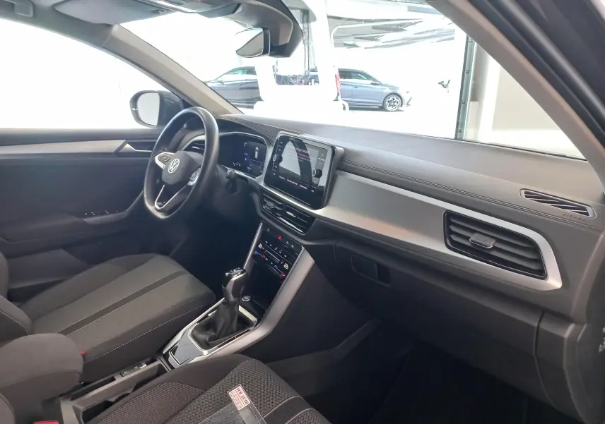 Vue intérieure côté conducteur du Volkswagen T-Roc 2025 gris Indium, avec tableau de bord moderne et écran tactile central.