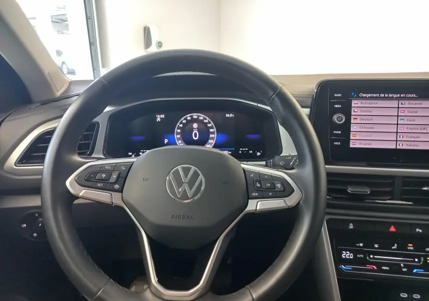 Vue intérieure centrée sur le volant du Volkswagen T-Roc gris Indium 2025 avec tableau de bord numérique et écran tactile.