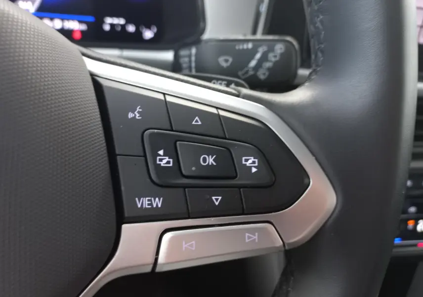 Gros plan sur les commandes multifonctions à gauche du volant du Volkswagen T-Roc 2025 gris Indium, avec boutons noirs et argentés.