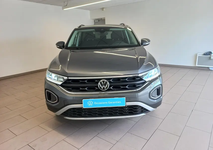 Vue avant d’un Volkswagen T-Roc 1.5 TSI 150 DSG7 VW Edition gris Indium avec calandre noire et feux LED allumés.