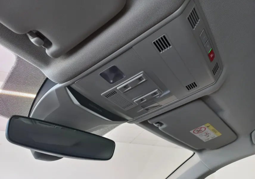 Vue intérieure du plafond avant du Volkswagen T-Roc 2025 gris Indium, montrant le miroir de courtoisie et les commandes d'éclairage.