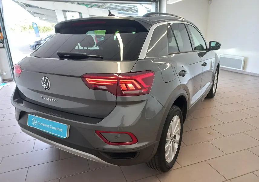 Vue 3/4 arrière droite d'un Volkswagen T-Roc gris Indium 2025 avec feux arrière LED et jantes alliage en showroom.