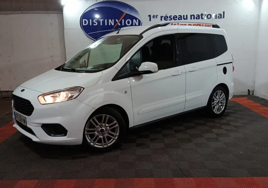Vue 3/4 avant droite d’un Ford Grand Tourneo Connect blanc avec phares allumés dans un showroom intérieur.