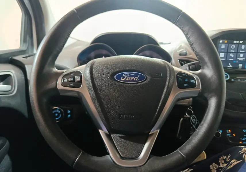 Vue rapprochée du volant cuir noir du Ford Grand Tourneo Connect 2020 avec tableau de bord et écran tactile en arrière-plan.