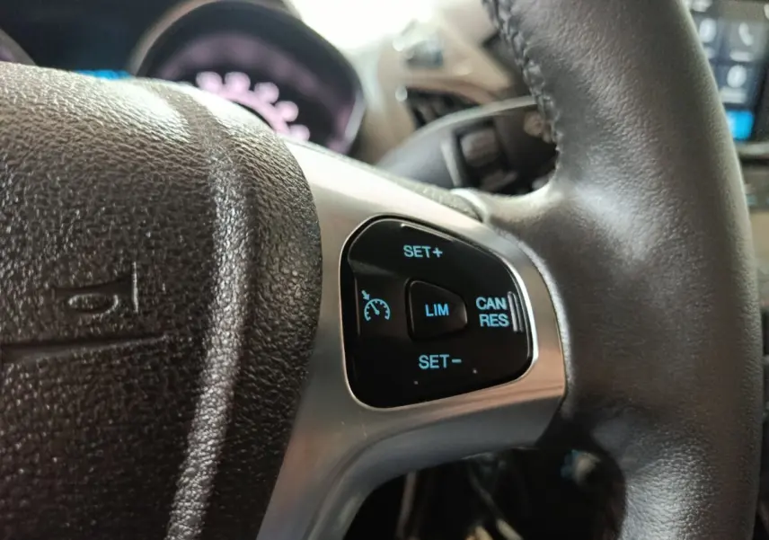 Gros plan sur les commandes du régulateur de vitesse au volant cuir noir du Ford Grand Tourneo Connect blanc.