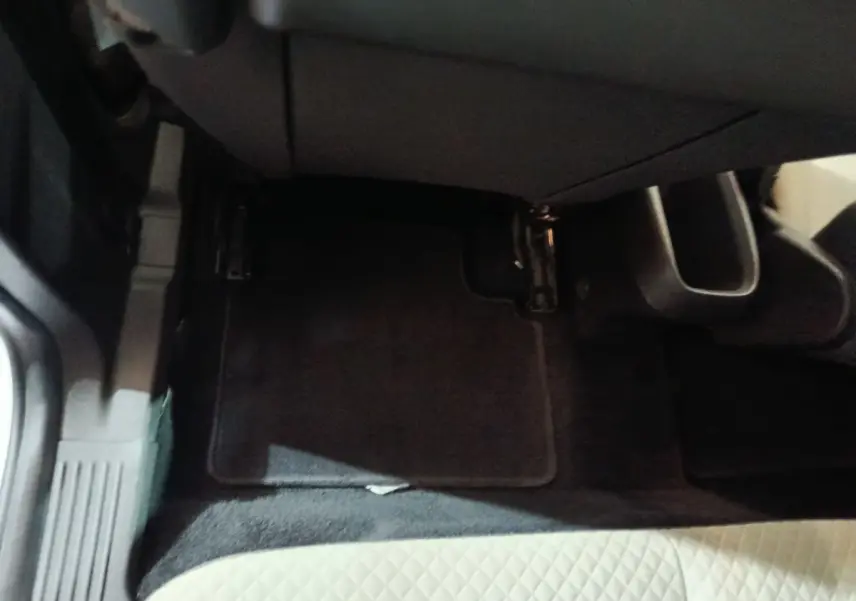 Vue rapprochée du plancher côté passager avant avec tapis noir et siège en tissu clair à motifs losanges.