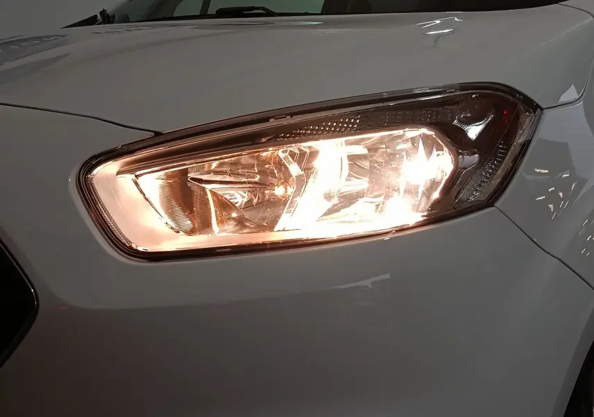 Gros plan sur le phare avant droit allumé d’un Ford Grand Tourneo Connect blanc, vue de face légèrement décalée.