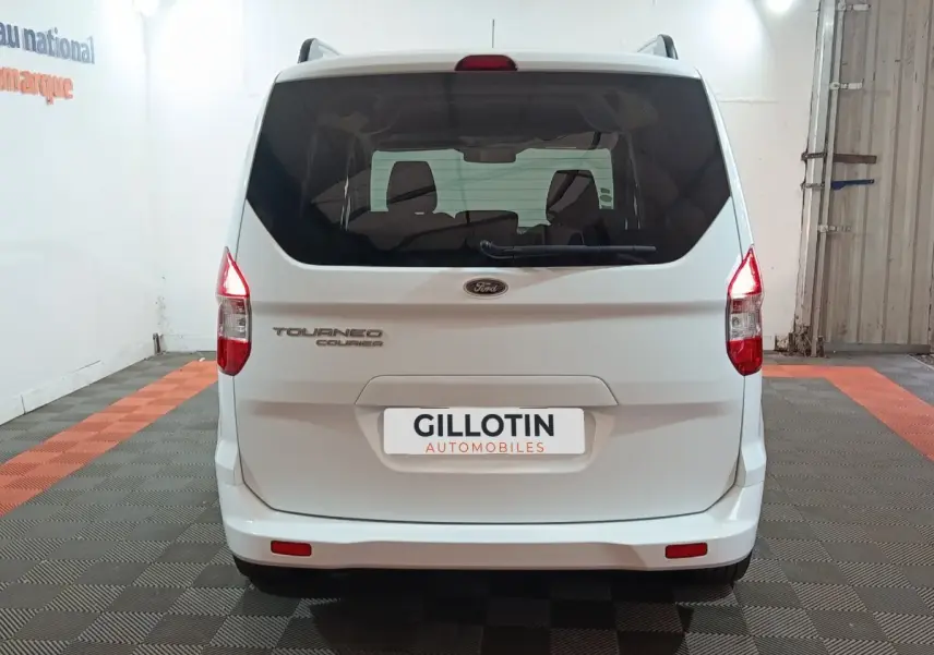Vue arrière d’un Ford Grand Tourneo Connect blanc, avec feux arrière allumés et logo visible sur un sol à damier.