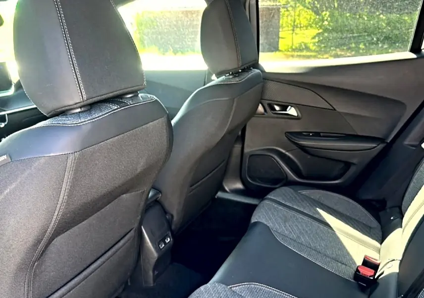 Vue intérieure arrière droite du Peugeot 2008 1.2 100 Allure 2025 avec sièges tissu noir et gris et portières noires.